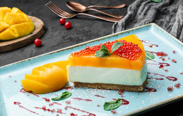 Wall Mural - Creamy mango cheesecake decorated with red berries and mint on a large plate and dark background, close up view. Summer desserts and sweets