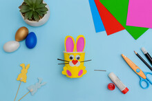 Happy Easter Day.Festive Craft From A Paper Cup With Your Own Hands.Leisure For Children.A Congratulatory Gift.Cute Yellow Easter Bunny On Blue Background