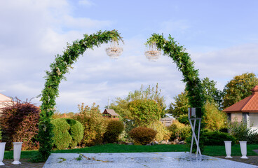 Wall Mural - Front view of minimalist greenery arch decorated with two chandeliers on the nature background.