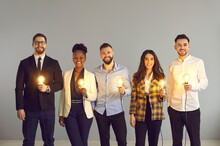 Teamwork And Brainstorming, Innovation Idea Creation And Share. Diverse Interracial Business Team Positive Smiling Holding Glowing Light Idea Bulb Standing Over Grey Copy Space Studio Background