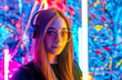 a young, attractive woman wearing headphones listens to music in the neon night light. girl DJ. Creative portrait in neon lighting. The concept of youth culture.