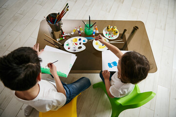 Two adorable children drawing and creating with watercolor paints at home. High angle view