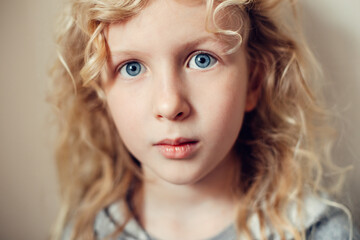 Wall Mural - Closeup portrait of beautiful pensive serious Caucasian blonde girl with long hair on light neutral beige background. Pretty real girl child with natural emotions. Happy authentic childhood lifestyle.