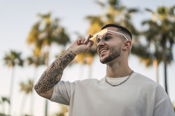 Wall Mural - Shallow focus shot of a handsome Spanish Caucasian man with tattoos and sunglasses posing outdoors