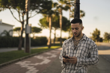 Poster - Shallow focus shot of a handsome Spanish Caucasian man with tattoos, using his phone outdoors