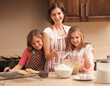 © Mike Kemp/Tetra Images - Portrait of mother baking with daughters (10-11) in kitchen