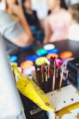 Wall Mural - Box of various paintbrushes with a watercolor set in the background