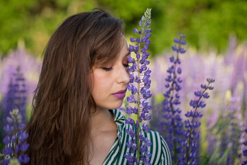 Gorgeous beautiful girl eyes closed Leans Head Against Lupin flower on blooming meadow, merging with natural beauty. healthy break, reconnecting with nature, digital detox concept. Sensual expression