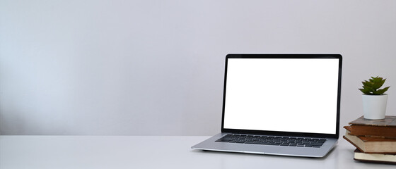 Horizontal photo of minimal workplace with computer laptop, plant and book on white desk.