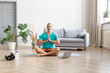 © Stavros - Photo of a middle-aged man taking an online yoga class. He is meditating sitting on the floor in front of a laptop monitor.