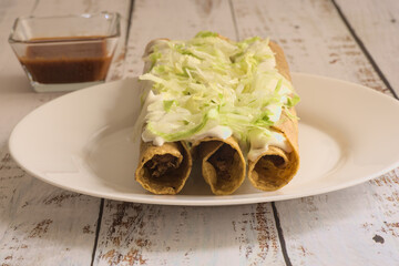 Traditional Mexican food, golden meat tacos (flautas) with red sauce.