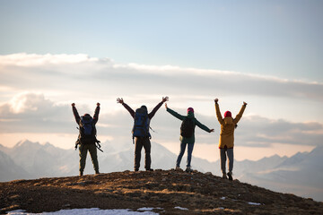 Wall Mural - Four young tourists with backpacks in winner poses at mountain top