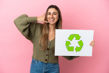 Wall Mural - Young caucasian woman isolated on pink background holding a placard with recycle icon and doing phone gesture