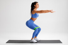 Fitness Woman Doing Squats Exercise For Glute With Resistance Band On Gray Background. Athletic Girl Working Out