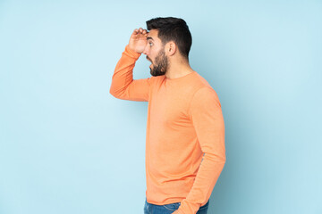 Caucasian handsome man with surprise expression while looking side over isolated blue background