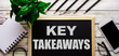 KEY TAKEAWAYS is written in white on a black board next to a phone, notepad, glasses, pencils and a green plant.