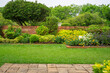 Backyard English cottage garden on brown pavement and green lawn