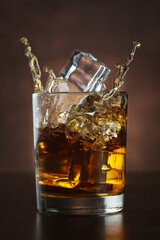 Wall Mural - Dropping ice cubes into a whiskey glass on a wooden background