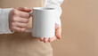 © Marykor - Female hands are holding a mockup of a white empty mug or cup of coffee tea, for your design and advertising, business concept on a beige background, Scandinavian style. Woman in white shirt