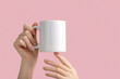 mockup white coffe cup or mug in female hands on pink background with copy space. Blank template for your design, branding, business. Real photo