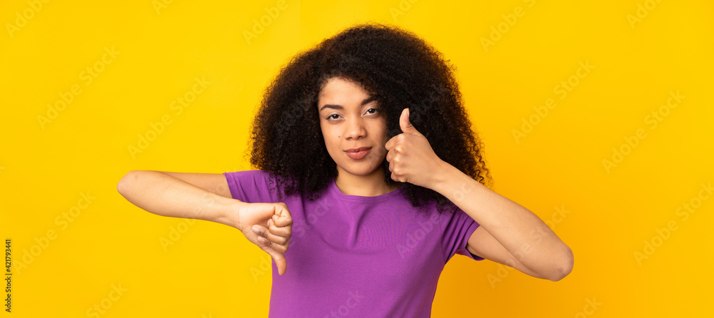 Young african american woman over isolated background making good-bad sign. Undecided between yes or not - obrazy, fototapety, plakaty 