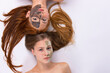 © Viorel - Two girls during spa procedures with clay masks on their faces lie on a white background with straightened long hair. Side white space.