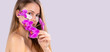 © Viorel - Banner, long format. Portrait of an attractive blonde girl with patches under the eyes posing with a branch of an orchid on a gray background.