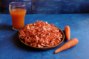 Carrot chips on a wooden plate on a blue background .  Two fresh carrots and a glass of carrot juice. Carrot chips are a favorite delicacy of children and ingredients for vegan and keto diets. 