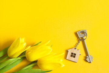 Wall Mural - Key ring in the shape of wooden house with key on yellow background and spring tulips. Building, design, project, moving to new home, mortgage, rent and purchase real estate, summer offer. Copy space