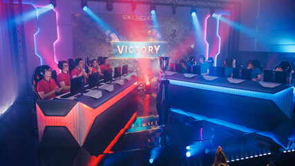 Wall Mural - Two Esport Teams of Pro Gamers Play in RPG Strategy Video Game on a Championship Arena, Happy Red Team Wins Round and Celebrates with High-Fives. Big Screen Showing Victory Sign. Cyber Games Event