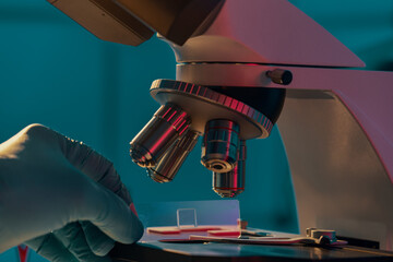 Poster - Glass slide with a tissue in hand and a scientific microscope. Screening biopsy sample in medical laboratory