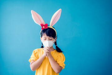 Happy easter day.Asian child girl mask in rabbit ears pray.Faith prayer Online worship in easter day home.Kid child medical mask.Healthcare, easter worship home church.Lockdown, covid19 coronavirus.