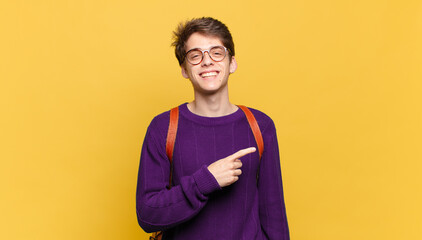 young student boy smiling cheerfully, feeling happy and pointing to the side and upwards, showing object in copy space