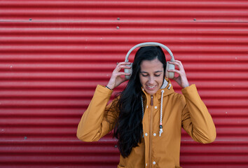 Girl in yellow raincoat listening to music leaning on a red wall