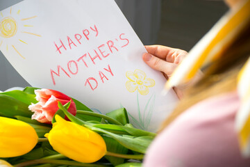 Happy Mother`s Day greeting card child's drawing and bouquet of flowers colorful tulips in mother`s hands. Lifestyle celebration or surprise for Mom on Mother`s Day.