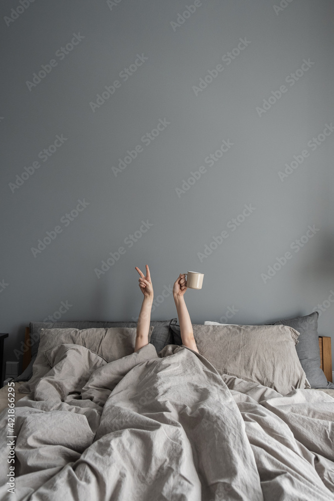Woman laying in bed and holding mug with coffee with hand and show "Victory" symbol. Happy morning breakfast concept. - obrazy, fototapety, plakaty 