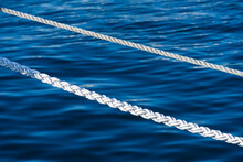 White Marine Mooring Rope Against Background Of Blue Water Of Black Sea. Two White Nautical Cord. Background Image Of Marine White Rope In Sochi Sea Port.