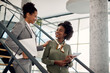 Happy black businesswoman talks to female mentor who leads her through office building.