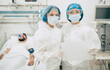© My Ocean studio - Two confident doctors in protective safety suits standing on background of a patient with coronavirus