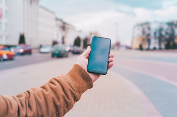 Wall Mural - A man holds a mock-up of a smartphone on the background of the road.