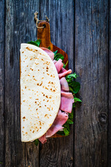 Wall Mural - Italian piada wraps - piadina stuffed with fresh vegetable leaves and prosciutto ham on wooden table