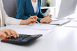 © Iryna - Accountant checking financial statement or counting by calculator income for tax form, hands close-up. Business woman sitting and working with colleague at the desk in office. Audit concept