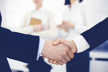 Businessman and woman shaking hands with colleagues at the background. Handshake at meeting in office. Concept of success in business