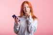 © Павел Костенко - Portrait of a pensive redhead girl with a smartphone in her hands in the studio on a pink background