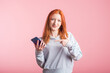 © Павел Костенко - Redhead girl points finger at smartphone in studio on pink background
