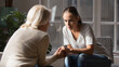 © fizkes - Supportive older Caucasian mom hold hands comfort caress talk with millennial female child feeling unhappy sad. Loving senior mother show support and care to upset depressed adult grownup daughter.