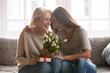 © fizkes - Loving young adult female child congratulate excited elderly mother with birthday anniversary at home. Smiling caring grownup millennial daughter present gift flowers to old mom on women s day.