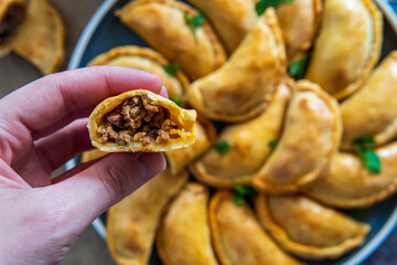 Hand holding Empanada cut into half with beef meat filling or stuffing. Traditional Latin American baked pastry and gluten free savory appetizer. Handmade typical dish in Spain or Argentina. top view