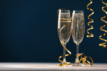 Glasses of champagne and serpentine streamers on table against dark blue background. Space for text