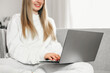 © Evgenia - A young blonde woman is sitting on the couch and using her laptop. Distance education. Work online. Freelancer girl